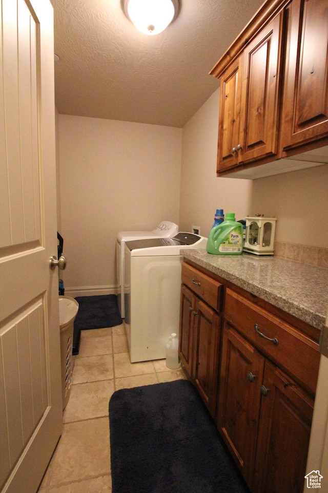 laundry room with a textured ceiling, light tile patterned flooring, baseboards, cabinet space, and washing machine and clothes dryer