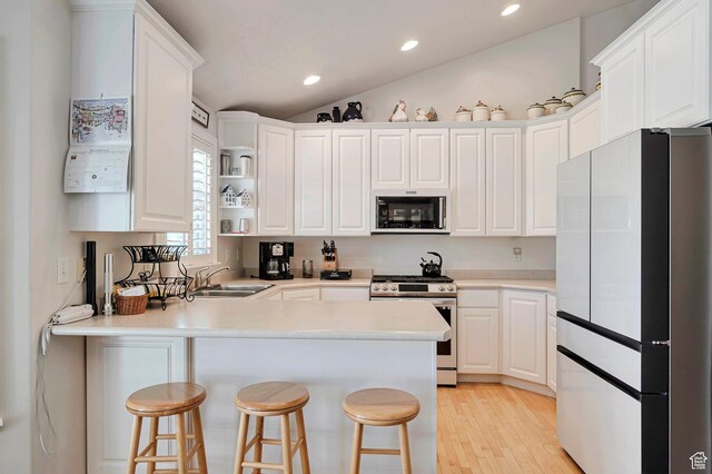 kitchen featuring freestanding refrigerator, a peninsula, stainless steel gas stove, light wood-type flooring, and a sink
