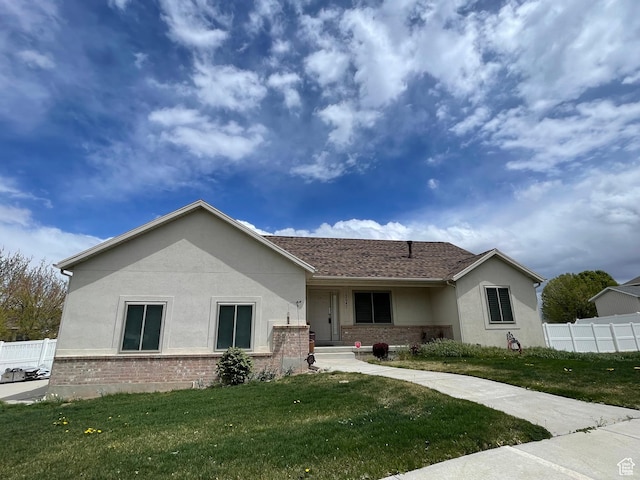 ranch-style home featuring stucco siding, a front lawn, fence, and brick siding