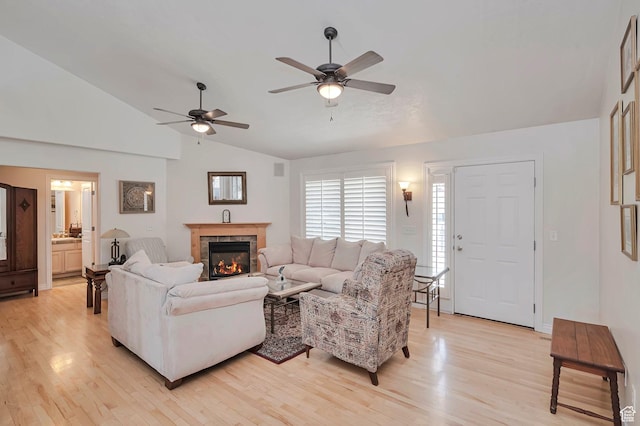 living area featuring ceiling fan, vaulted ceiling, light wood-style flooring, and a fireplace