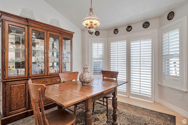 dining area with light wood-style floors, baseboards, a notable chandelier, and lofted ceiling