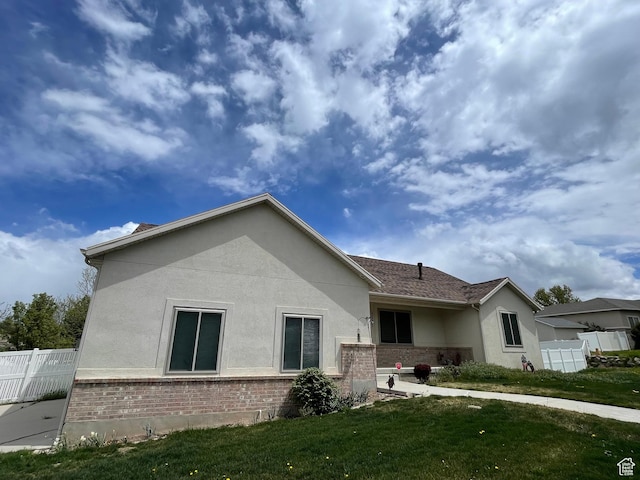 view of home's exterior with fence, stucco siding, a lawn, and brick siding
