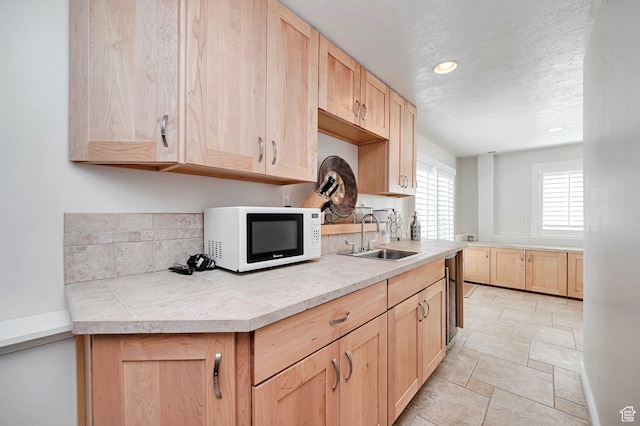 kitchen with a textured ceiling, light brown cabinetry, a sink, white microwave, and stone tile flooring