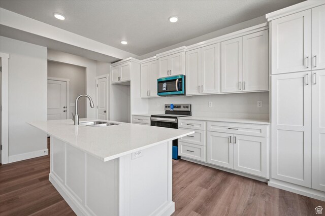kitchen featuring dark wood finished floors, an island with sink, stainless steel appliances, a sink, and light countertops