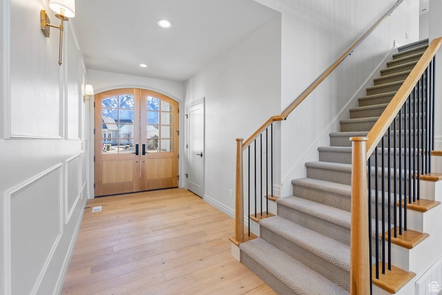 foyer with arched walkways, light wood-style flooring, recessed lighting, french doors, and stairway