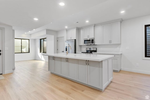 kitchen featuring light countertops, appliances with stainless steel finishes, light wood-type flooring, and a kitchen island with sink
