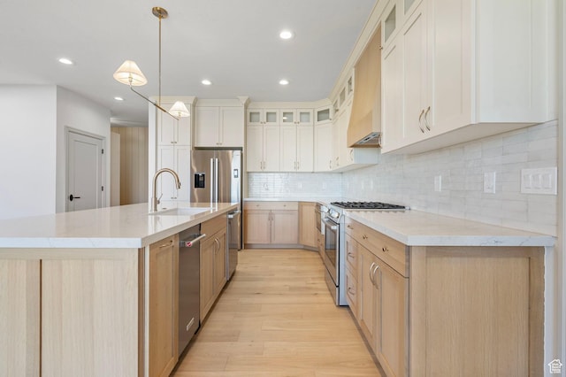 kitchen featuring light wood-style flooring, decorative backsplash, appliances with stainless steel finishes, glass insert cabinets, and a sink