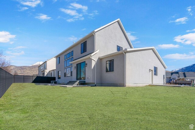 rear view of house featuring fence, a lawn, and stucco siding