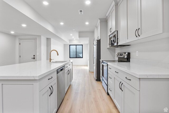 kitchen featuring stainless steel appliances, recessed lighting, light wood-style floors, a sink, and an island with sink