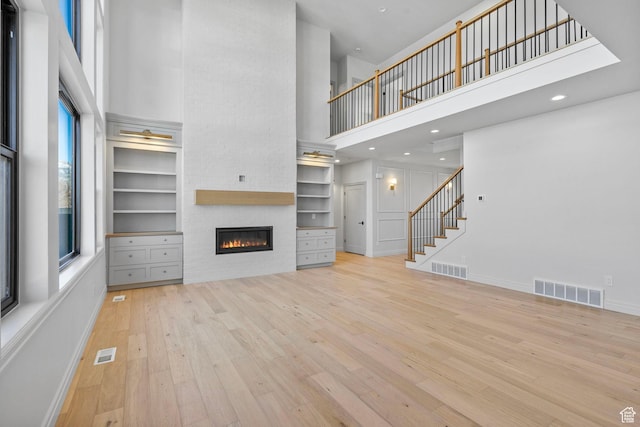 unfurnished living room featuring stairs, visible vents, a high ceiling, and hardwood / wood-style flooring