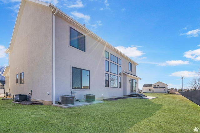 rear view of property with stucco siding, fence, cooling unit, and a yard