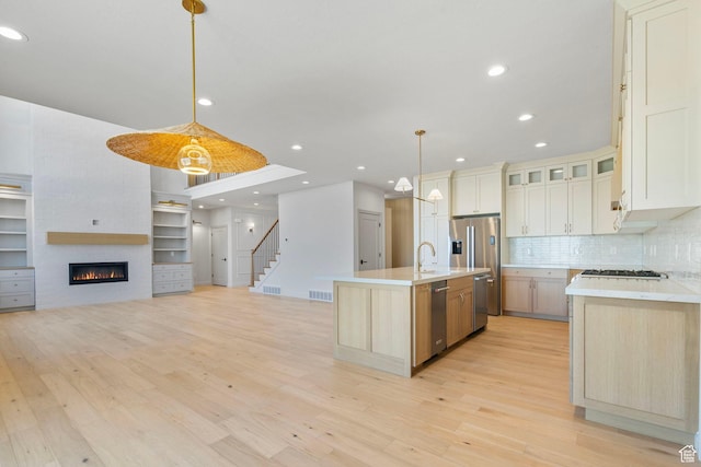 kitchen with light wood finished floors, light countertops, appliances with stainless steel finishes, and a kitchen island with sink