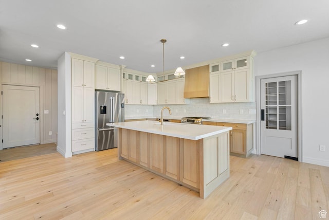 kitchen featuring light wood-style flooring, light countertops, appliances with stainless steel finishes, backsplash, and custom range hood