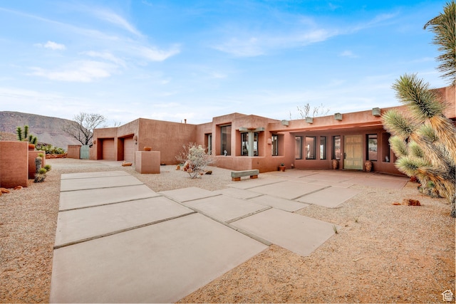 rear view of house featuring a mountain view, an attached garage, driveway, and stucco siding