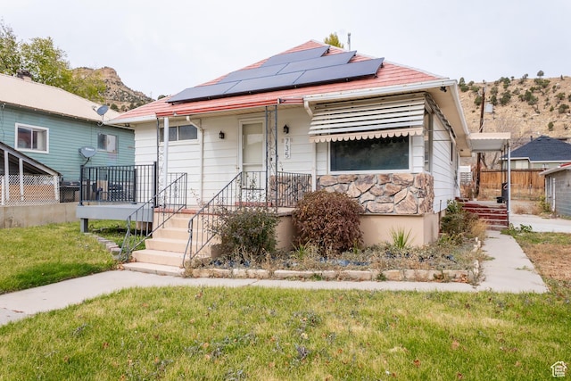 bungalow with stone siding, a front lawn, and roof mounted solar panels