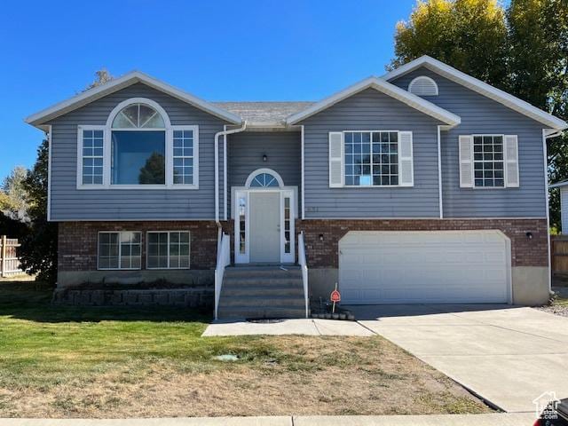 bi-level home with an attached garage, a front lawn, concrete driveway, and brick siding