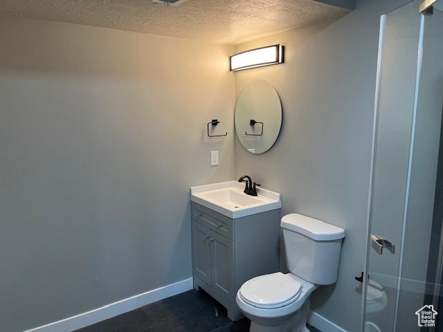 full bath with baseboards, toilet, a shower with door, a textured ceiling, and vanity