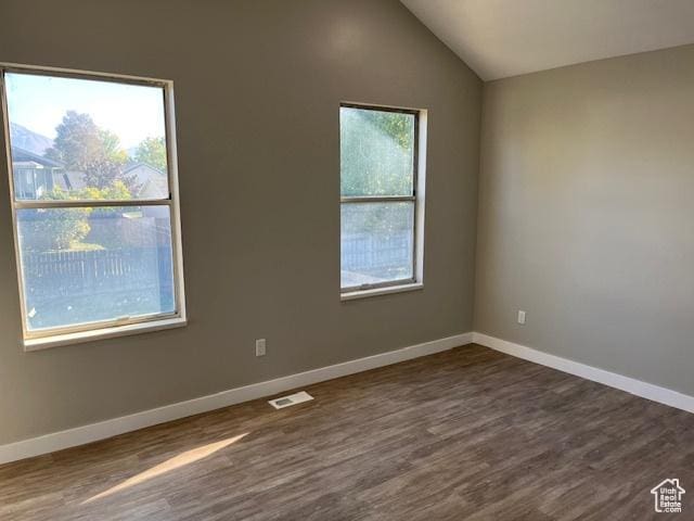 unfurnished room with dark wood-style flooring, visible vents, vaulted ceiling, and baseboards