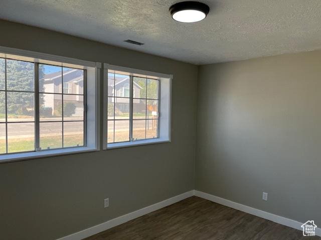 empty room featuring a textured ceiling, baseboards, and dark wood-type flooring