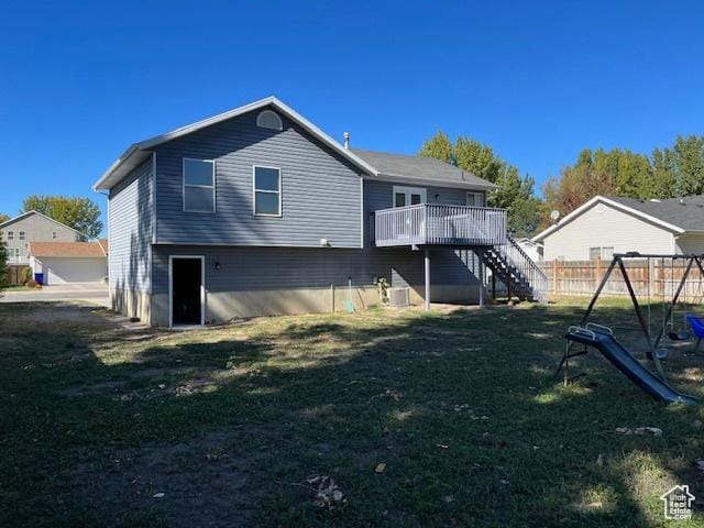 back of house featuring a playground, a lawn, stairway, fence, and a deck