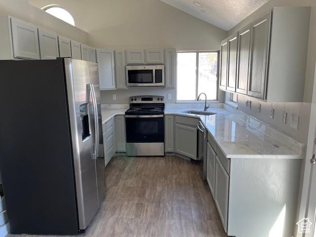 kitchen with lofted ceiling, a textured ceiling, a sink, appliances with stainless steel finishes, and light wood finished floors