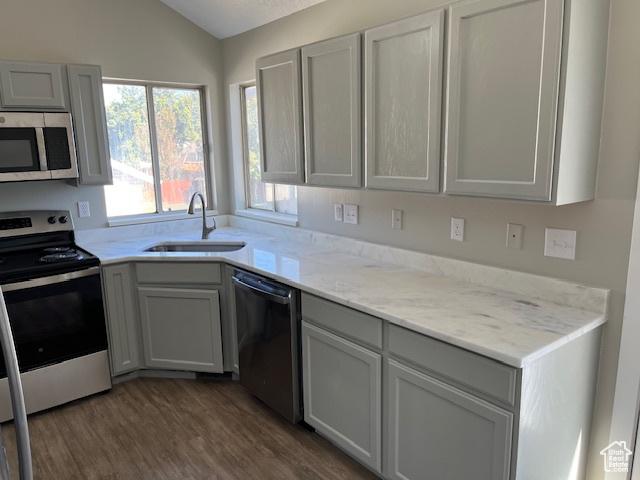 kitchen with lofted ceiling, gray cabinetry, a sink, appliances with stainless steel finishes, and dark wood-style floors