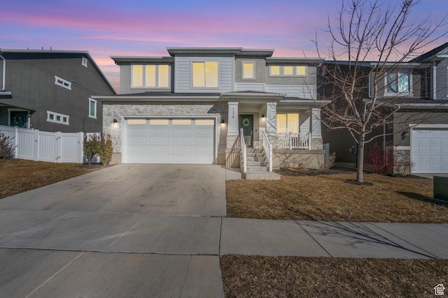 view of front of home featuring concrete driveway, stone siding, an attached garage, a gate, and fence
