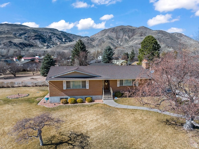 view of front of property with a front yard, brick siding, a mountain view, and a chimney