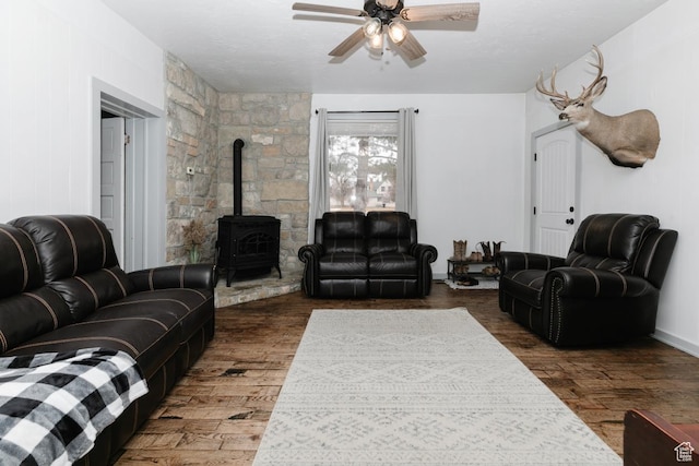 living room featuring a ceiling fan, a wood stove, and wood finished floors