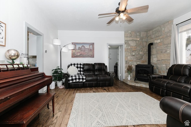 living area featuring a ceiling fan, a wood stove, and wood finished floors