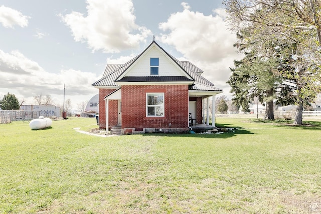 rear view of property featuring brick siding, fence, a yard, and metal roof