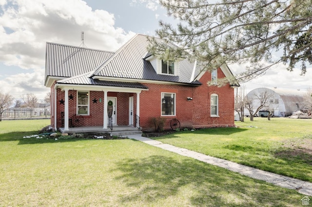 view of front of home with brick siding, covered porch, a front yard, and metal roof