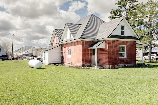 view of side of property with a mountain view, metal roof, brick siding, entry steps, and a yard