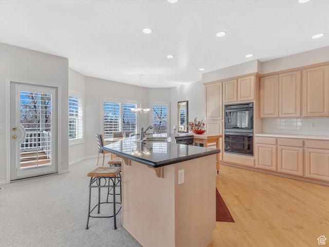 kitchen featuring dobule oven black, tasteful backsplash, a breakfast bar, light brown cabinets, and a sink