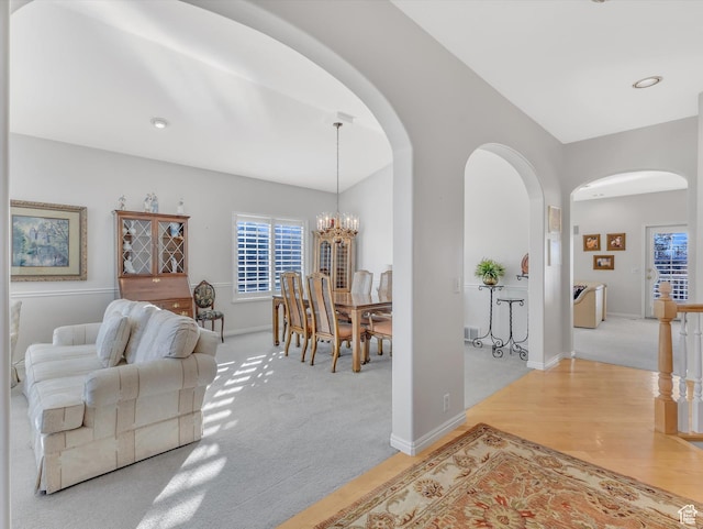 living area with a chandelier, arched walkways, wood finished floors, carpet flooring, and baseboards
