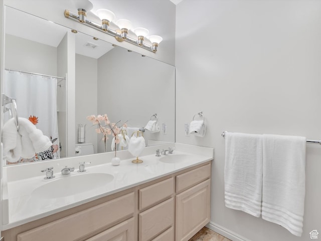 bathroom featuring visible vents, double vanity, a sink, and toilet
