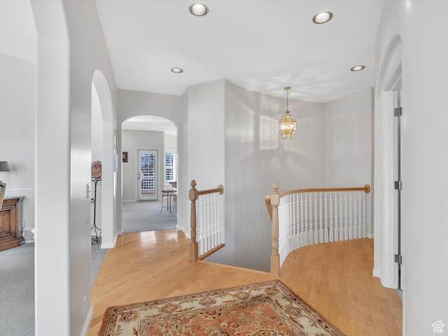 hallway with light wood-type flooring, arched walkways, an upstairs landing, and recessed lighting