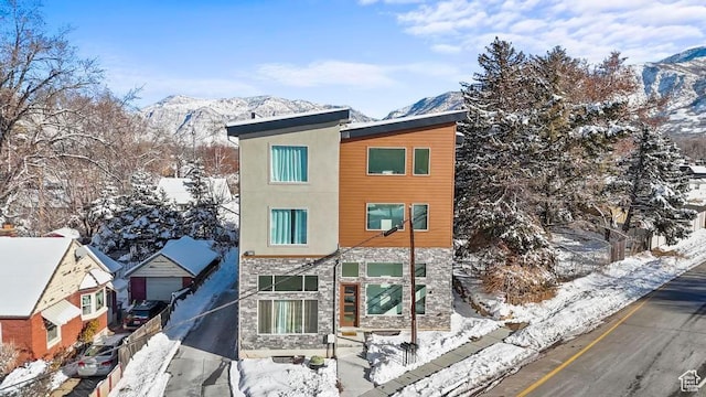 snow covered property featuring stone siding, a mountain view, and stucco siding