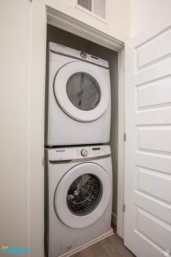 clothes washing area featuring laundry area, wood finished floors, visible vents, and stacked washer / drying machine