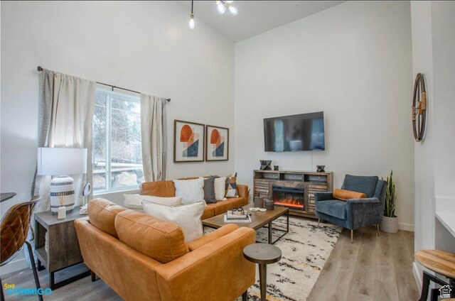 living area with high vaulted ceiling, a stone fireplace, baseboards, and wood finished floors