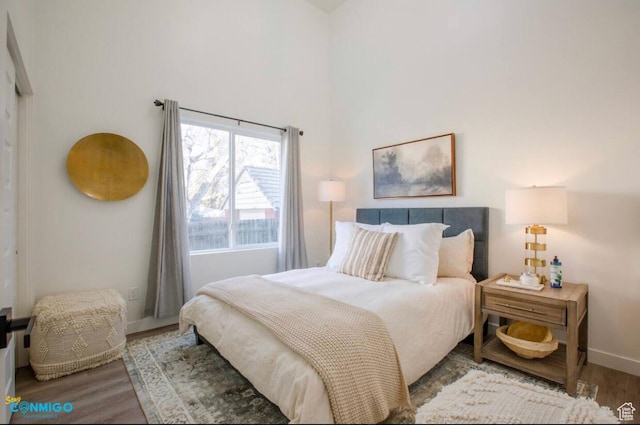 bedroom featuring a towering ceiling, baseboards, and wood finished floors