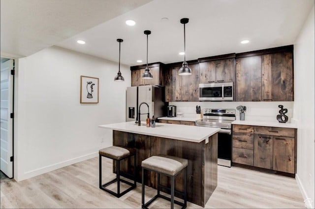 kitchen with stainless steel appliances, a breakfast bar, light countertops, light wood finished floors, and a center island with sink