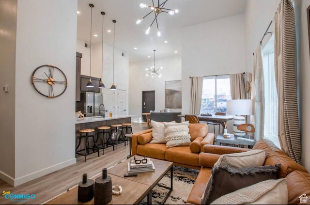 living room featuring a notable chandelier, recessed lighting, light wood-style flooring, a towering ceiling, and baseboards