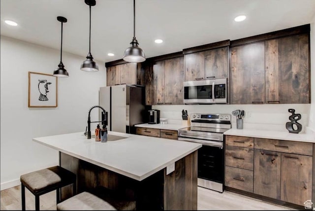 kitchen featuring a center island with sink, stainless steel appliances, light countertops, light wood-type flooring, and a sink