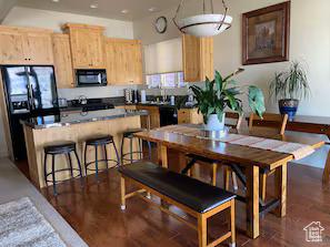3435 Big Piney Dr, Eden, UT 84310 - kitchen with dark countertops, dark wood-style floors, light brown cabinetry, black appliances, and a kitchen bar