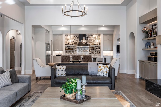 living area with arched walkways, a chandelier, wood finished floors, and baseboards