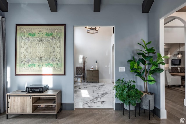 interior space with arched walkways, beam ceiling, an inviting chandelier, wood finished floors, and baseboards