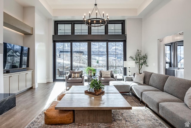 living area with a towering ceiling, a chandelier, a raised ceiling, and wood finished floors