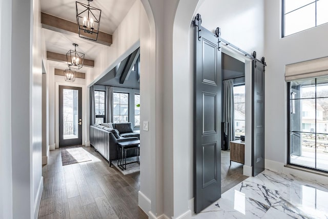 foyer entrance with baseboards, a healthy amount of sunlight, an inviting chandelier, and a barn door