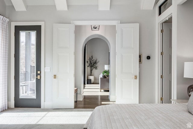 bedroom featuring access to exterior, arched walkways, beam ceiling, and wood finished floors